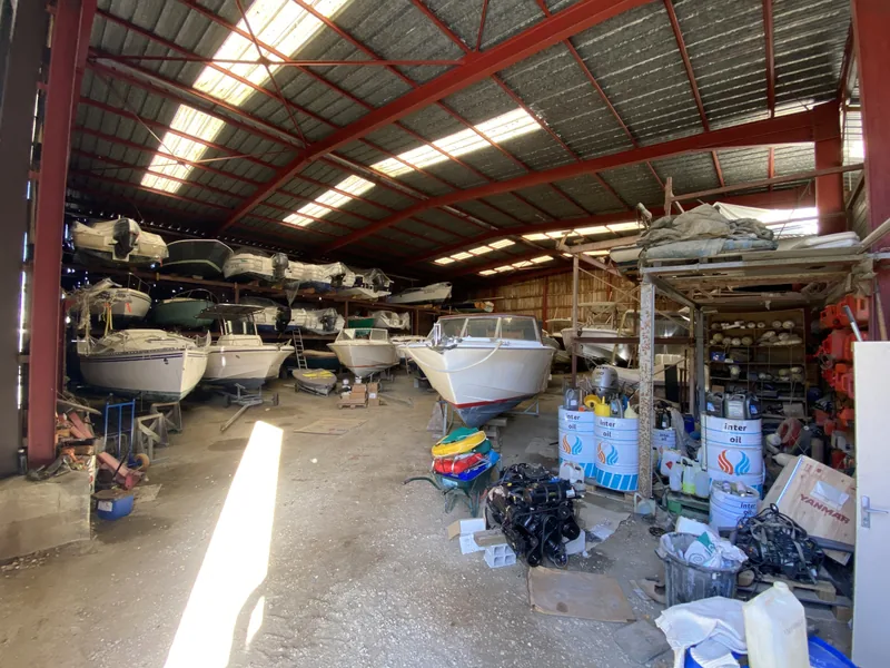 L’intérieur du hangar : bateaux sur racks, moteurs et bidons d’huile